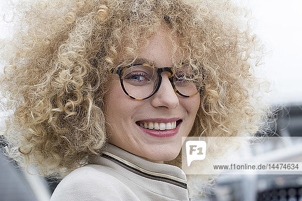 Porträt einer lächelnden blonden Frau mit Ringellocken und einer modischen Brille