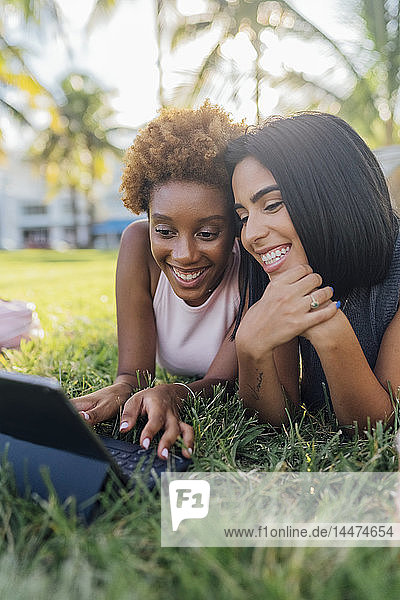 Portrait of two happy female friends relaxing in a park using a tablet