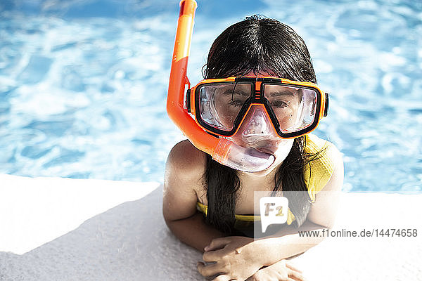 Porträt eines kleinen Mädchens mit Schnorchel und übergroßer Taucherbrille  das sich am Beckenrand anlehnt
