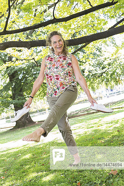 Porträt einer glücklichen reifen Frau  die barfuss auf einer Wiese in einem Park steht