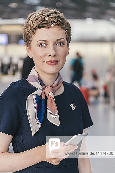 Porträt eines selbstbewussten Mitarbeiters einer Fluggesellschaft  der sein Handy am Flughafen in der Hand hält