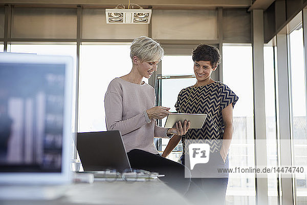 Two smiling businesswomen sharing tablet in office