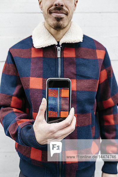 Junger Mann zeigt am Telefon ein Foto in den Farben seiner Jacke