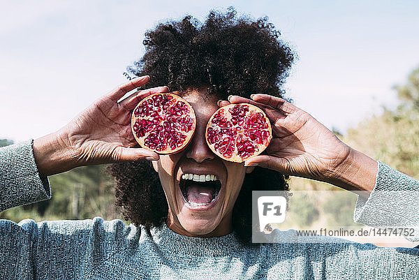 Woman standing in the countryside  covering eyes with halved pomegranates