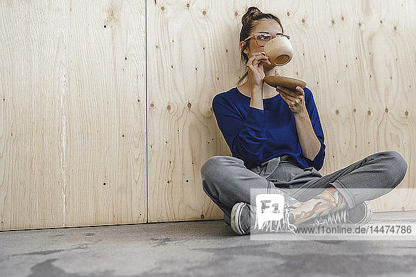 Junge Frau macht eine Pause im Büro und trinkt Kaffee aus einer Holztasse