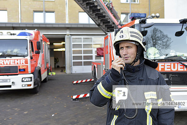 Firefighter standing on yard at fire engine using walkie talkie