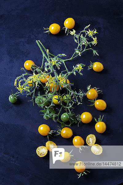 Whiole und in Scheiben geschnittene Tomaten 'Blondköpfchen' auf dunklem Grund