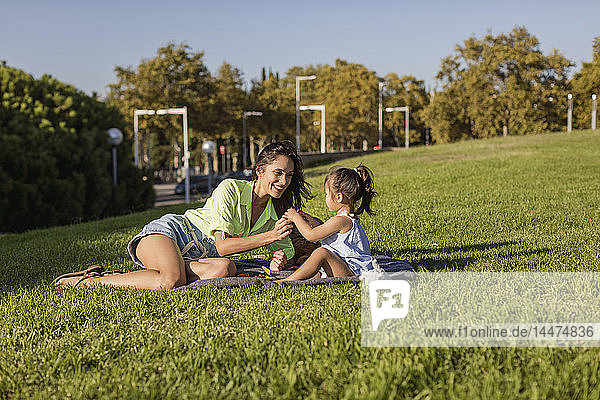 Glückliche Mutter spielt mit Tochter auf einer Decke im Park