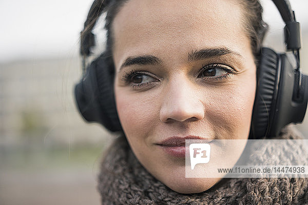 Porträt einer lächelnden Frau mit Schal  die mit schnurlosen Kopfhörern Musik hört  Nahaufnahme