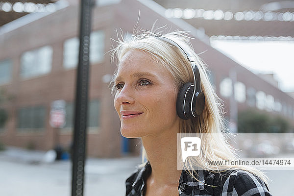 USA  New York City  Brooklyn  lächelnde junge Frau  die in der Stadt mit Kopfhörern Musik hört