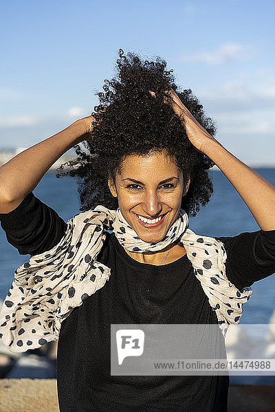 Porträt einer lächelnden Frau mit wehendem Schal und Händen im Haar