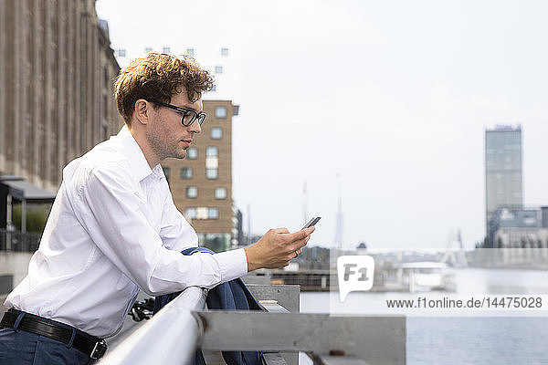 Deutschland  Berlin  Geschäftsmann lehnt sich an die Reling und schaut auf das Smartphone