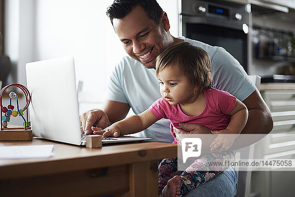 Smiling father and baby girl using laptop on table at home
