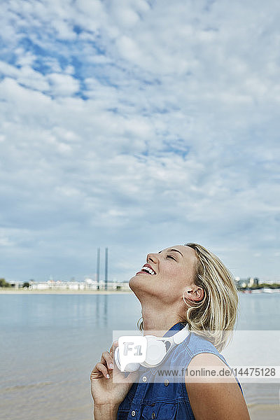 Deutschland  Düsseldorf  glückliche junge Frau mit Kopfhörern am Rheinufer