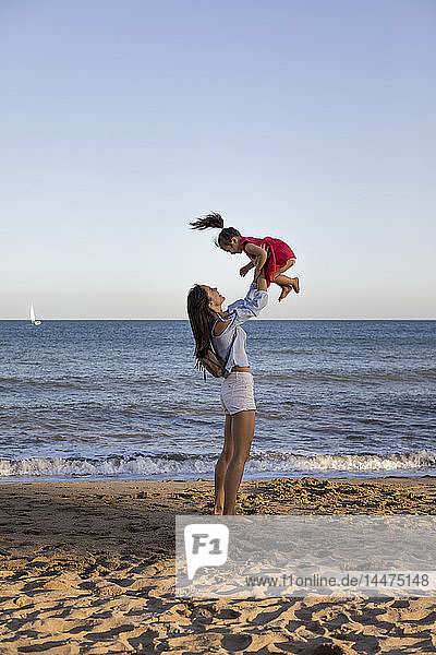Mutter und Tochter amüsieren sich am Strand und tun so  als würden sie fliegen