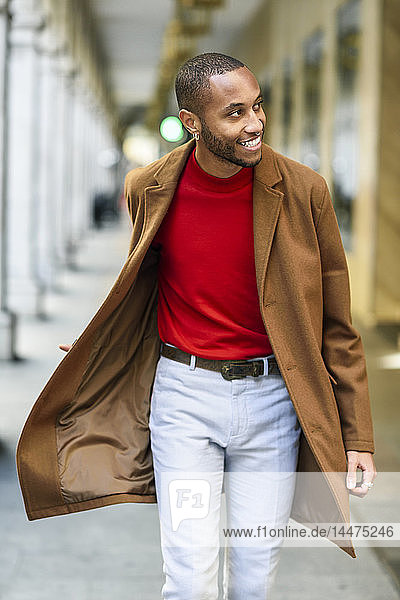 Fashionable young man wearing red pullover and brown coat walking along arcade