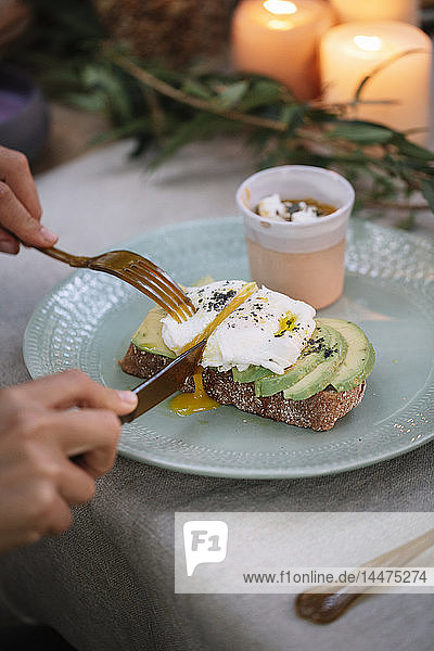 Close-up of woman cutting bread with avocado on garden table with candles