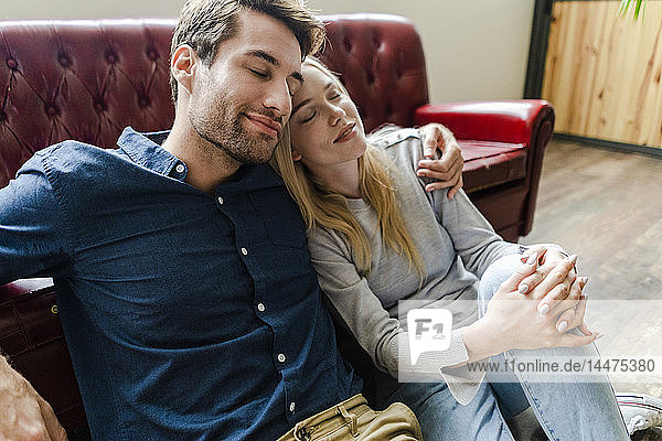 Lächelndes junges Paar mit geschlossenen Augen sitzt auf dem Boden und umarmt