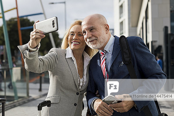Leitender Geschäftsmann und Geschäftsfrau mit Gepäck  die sich in der Stadt ein Selfie nehmen