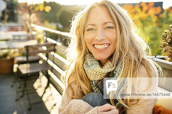 Porträt einer glücklichen blonden  reifen Frau auf dem Balkon im Herbst