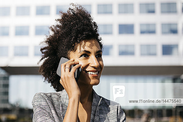 Porträt einer lächelnden Geschäftsfrau am Mobiltelefon vor dem Bürogebäude
