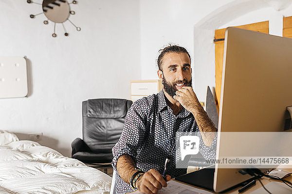 Lächelnder junger Mann arbeitet zu Hause am Computer
