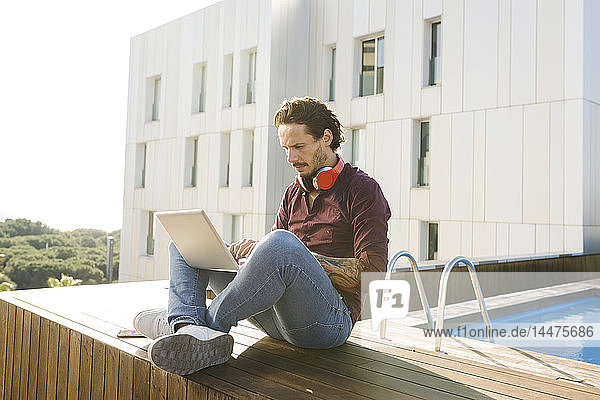 Man sitting cross-legged on a rooftop terrace  using laptop  wearing headphones