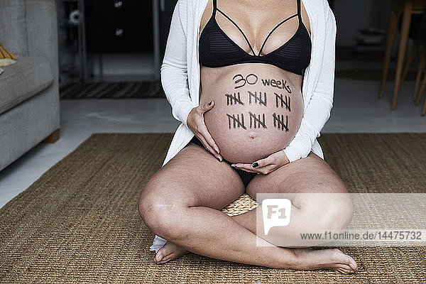 Nahaufnahme einer schwangeren Frau  die zu Hause auf dem Boden sitzt und Striche auf dem Bauch hat