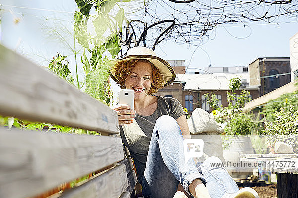Lächelnde junge Frau mit Strohhalm und Smartphone im Stadtgarten
