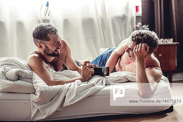 Happy gay couple with old-fashioned camera in bed