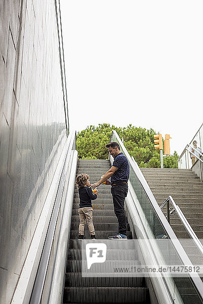 Vater und Sohn mit Erfrischungsgetränken auf der Rolltreppe