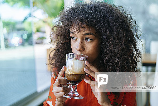 Portrait of young woman drinking coffee in a cafe while looking out of window