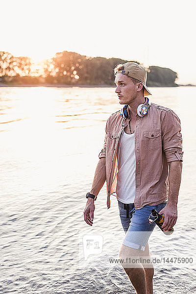 Junger Mann geht bei Sonnenuntergang am Flussufer