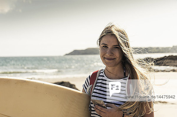 Junge Frau am Strand  die ein Surfbrett trägt