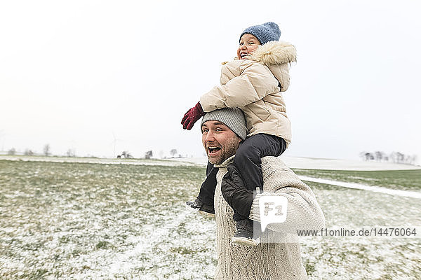 Playful father carrying daughter piggyback in winter landscape