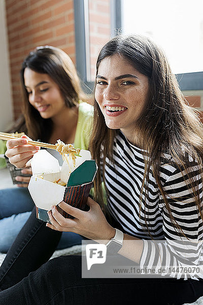 Zwei glückliche junge Frauen essen zu Hause asiatisches Essen zum Mitnehmen