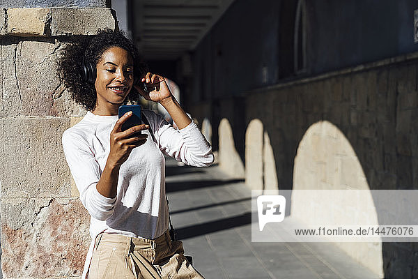 Young casual businesswoman with smartphone and earphones in the city