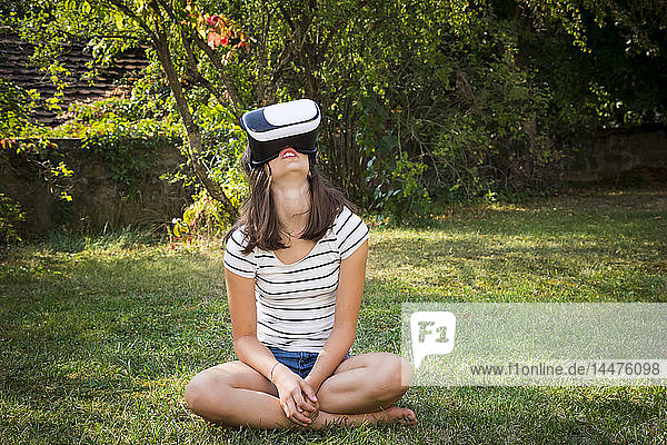 Girl sitting on meadow in the garden using Virtual Reality Glasses