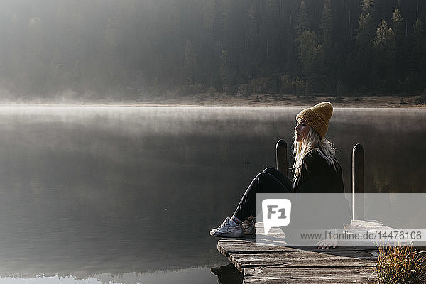 Switzerland  Engadine  Lake Staz  woman sitting on a jetty at lakeside in morning sun