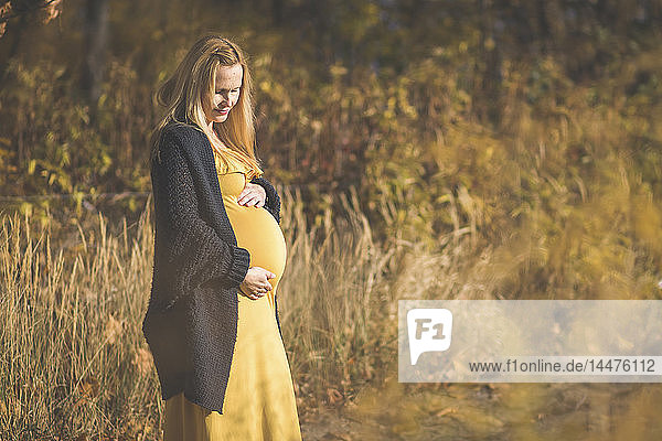 Schwangere Frau steht im Herbst auf Waldpfad