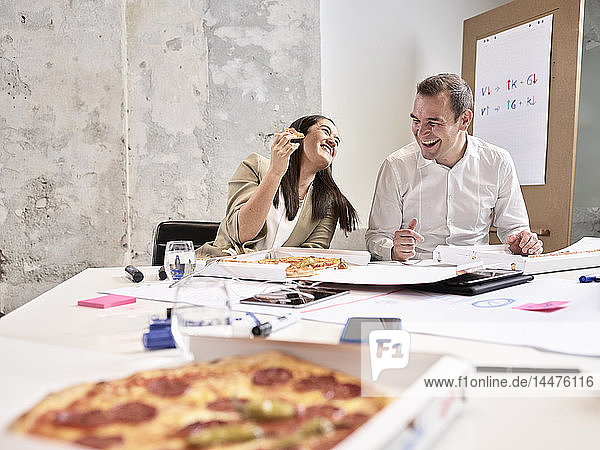 Lachende Kollegen machen Mittagspause mit Pizza im Konferenzraum