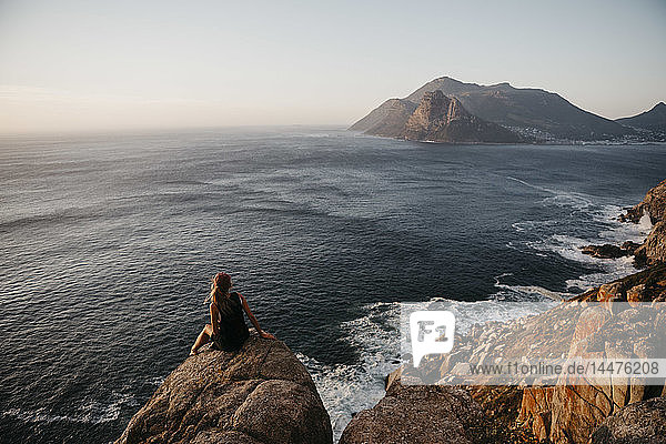 Südafrika  Westkap  Frau sitzt auf einem Felsen und schaut auf die Aussicht  gesehen vom Chapman's Peak Drive
