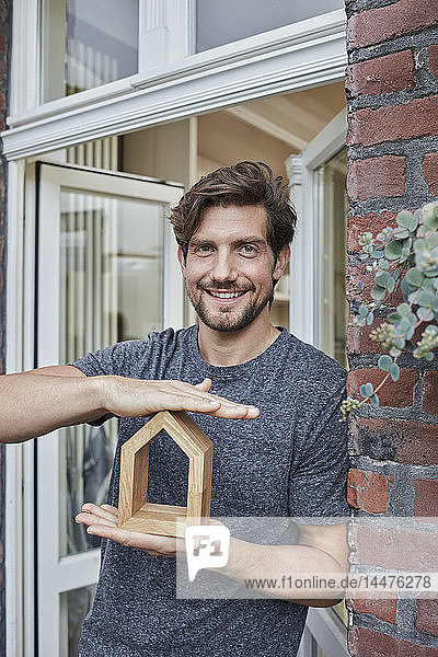 Porträt eines lächelnden Mannes am Hauseingang  der ein Hausmodell hält