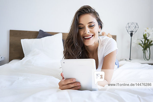 Junge Frau liegt im Bett  benutzt digitales Tablett  liest
