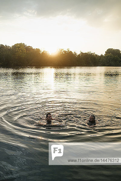 Alter und junger Mann schwimmen bei Sonnenuntergang in einem See