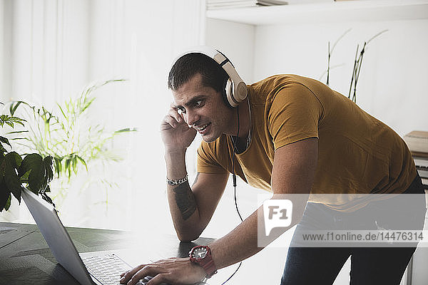 Lächelnder junger Mann mit Kopfhörern und Laptop