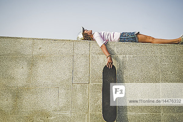 Mädchen mit Skateboard an der Wand liegend
