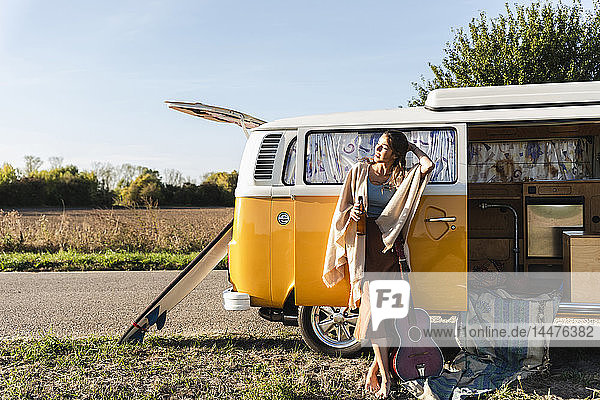 Hübsche Frau auf einer Autoreise mit ihrem Wohnwagen  Bier trinkend  Gitarre haltend