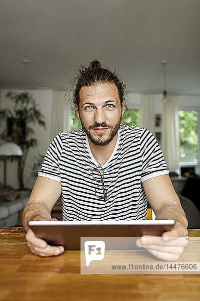 Young man with a bun sitting at home  using digital tablet