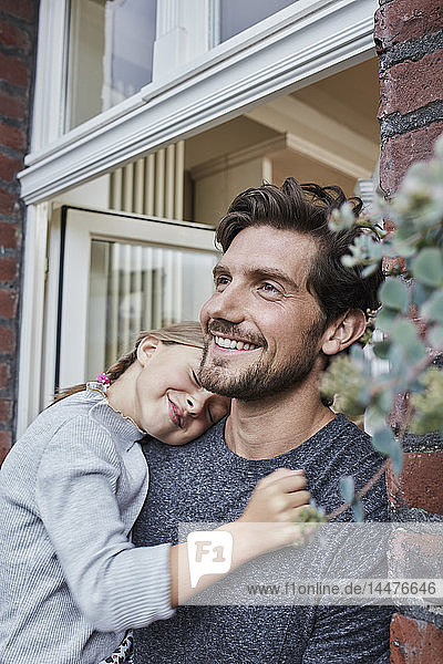Lächelnder Vater mit Tochter am Hauseingang ihres Hauses